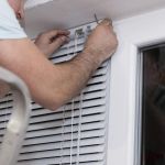 A handyman in a uniform installing new window blinds in the residential or business apartment. Worker providing blind curtain mounting. Professional service - home repair and renovation works